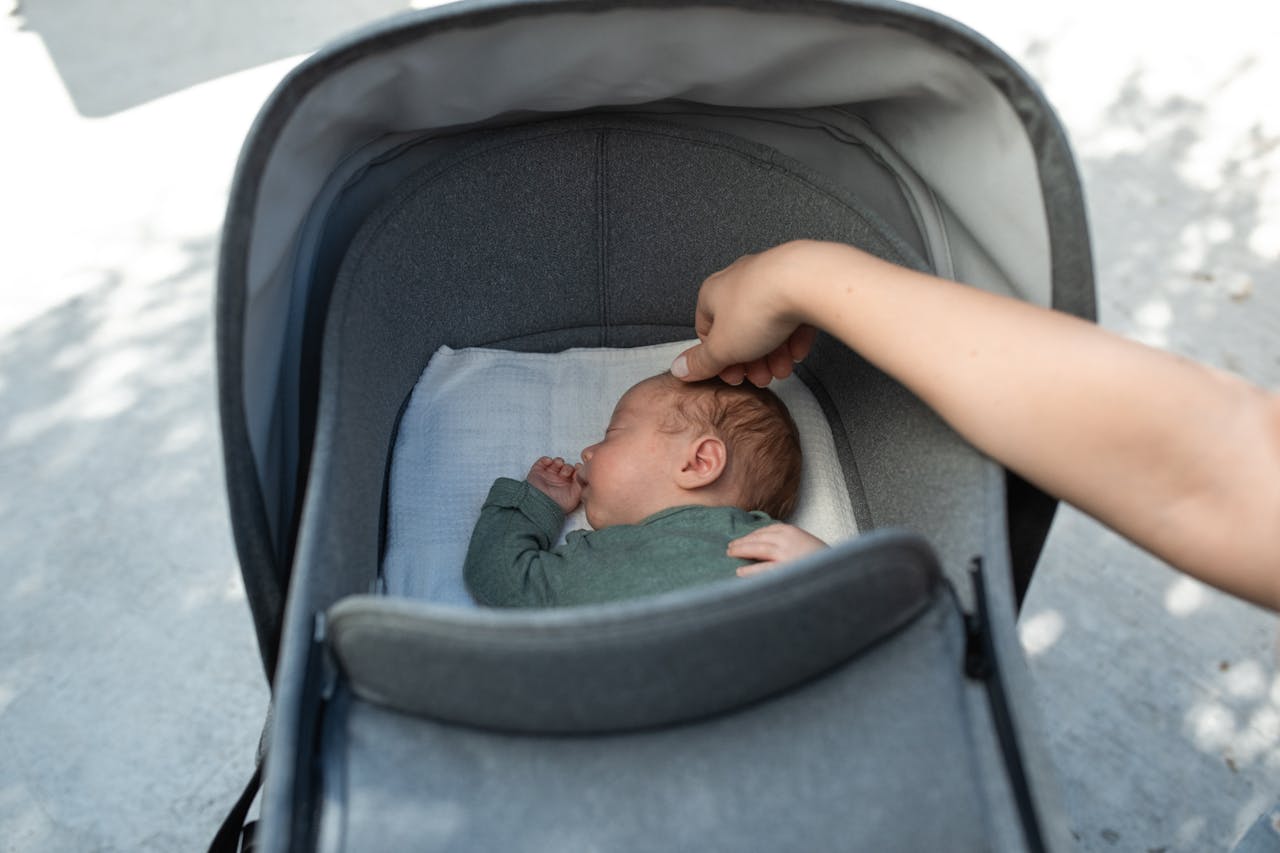 A serene moment of a baby sleeping in a stroller with a gentle touch from an adult hand.