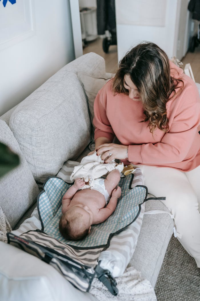 A serene moment of a mother changing her baby's diaper on a sofa at home.